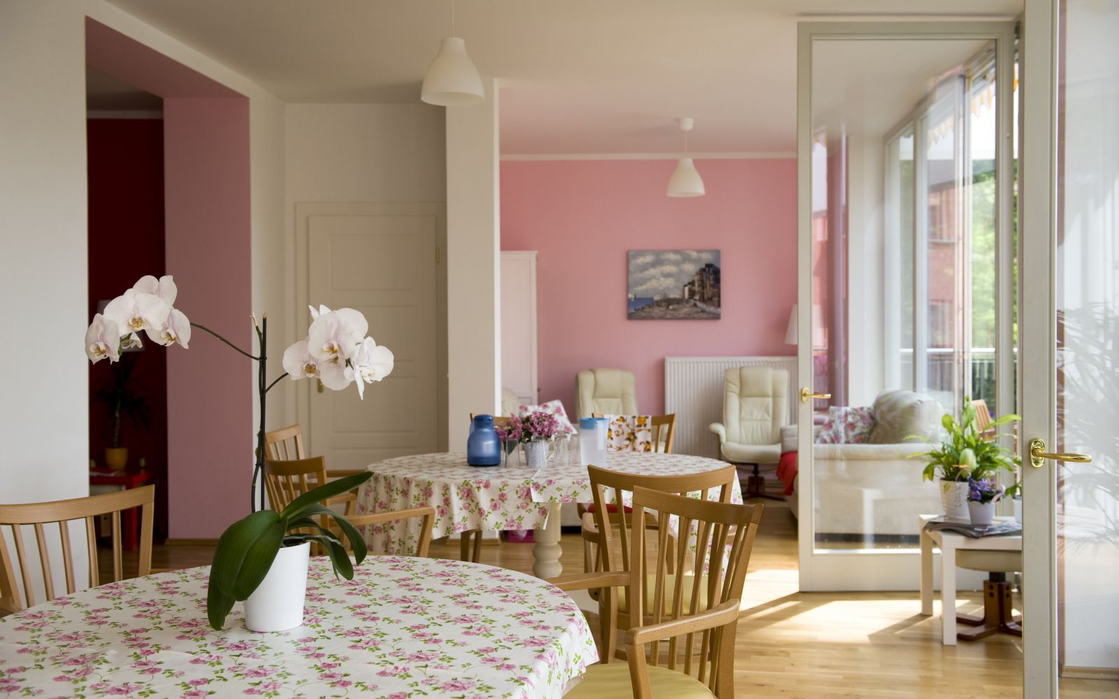 Stühle und Tische in lichtdurchfluteten Raum mit rosanen Wänden.